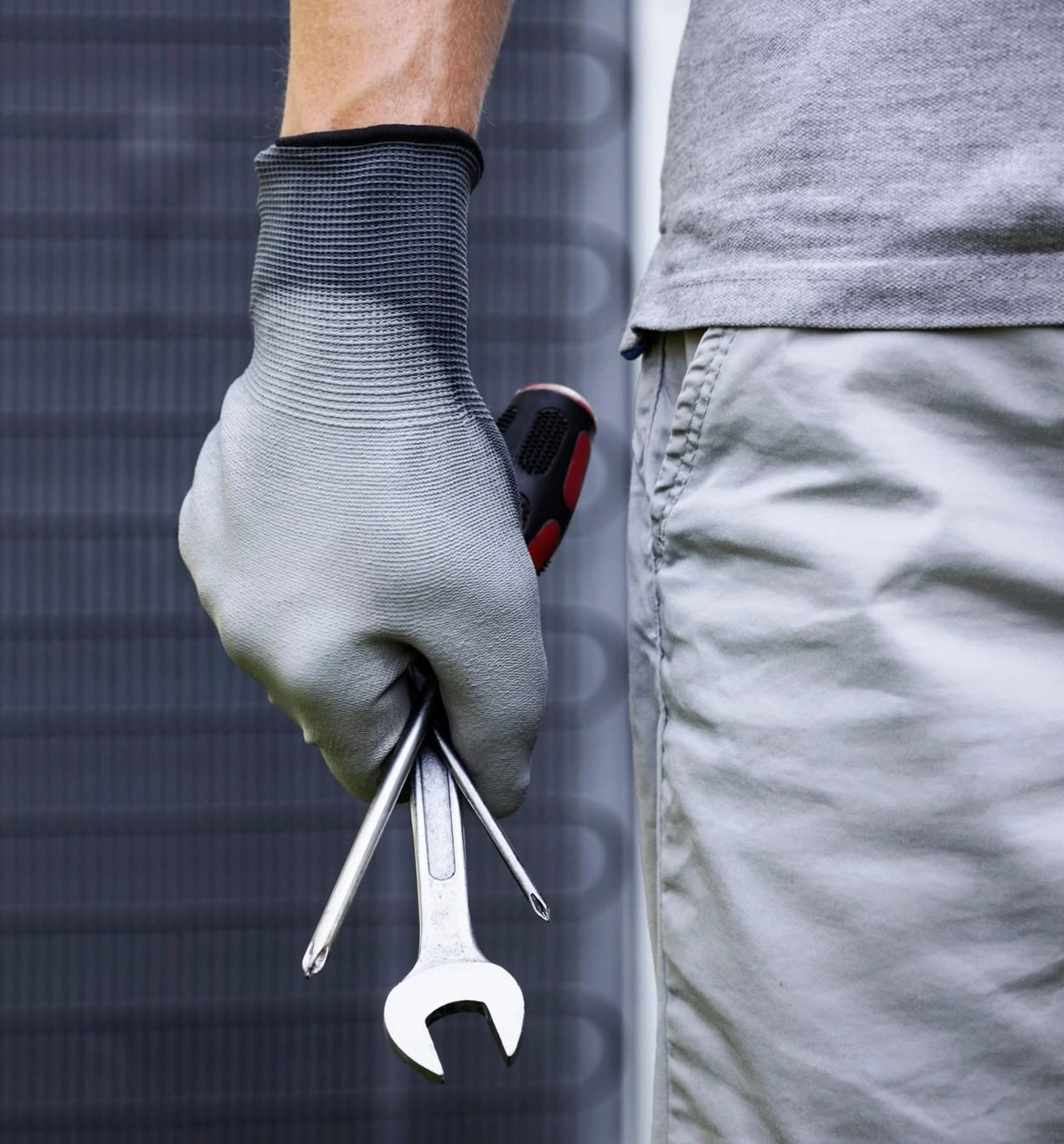 Person wearing gray gloves holds a wrench and screwdriver next to their shorts, ready for work.