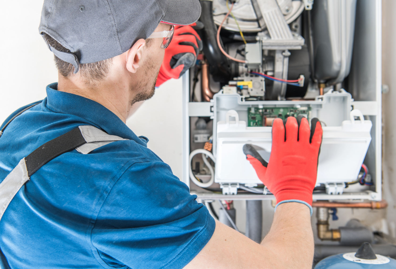 Technician in red gloves repairs open boiler unit, examining circuit board and wiring connections.