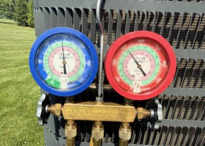 Blue and red HVAC pressure gauges connected to an outdoor air conditioning unit.