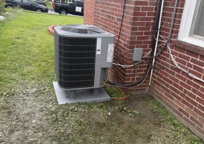 An outdoor central air conditioning unit sitting on a pad next to a brick house.