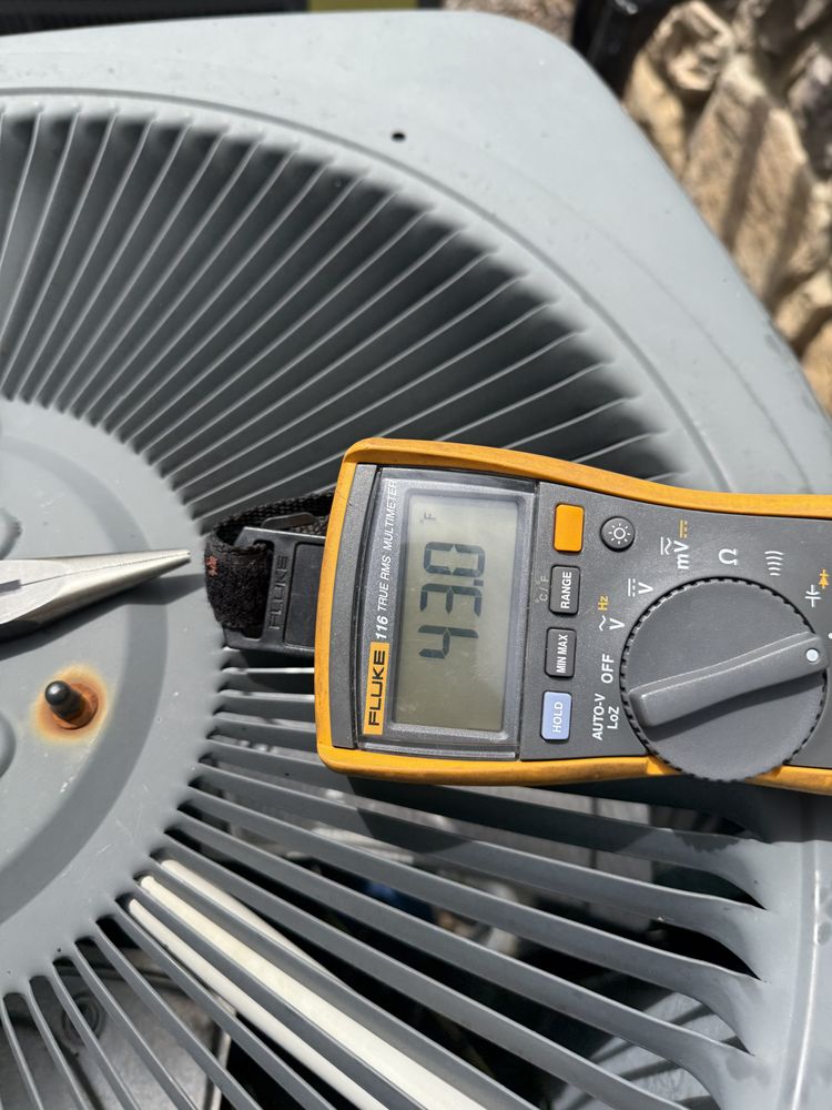 A digital multimeter displays 49.4 on top of a gray air conditioning unit with metal fan blades.