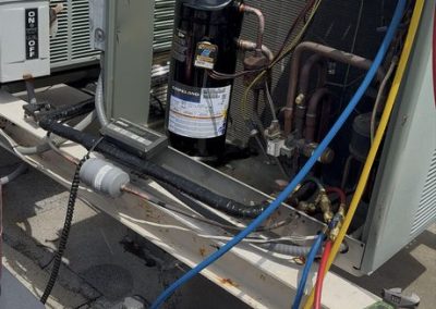 HVAC unit on a rooftop being serviced with gauge manifold hoses and a vacuum pump.
