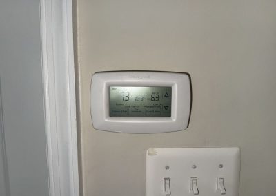 Honeywell digital thermostat on a wall above a light switch plate.