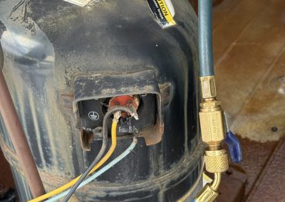 Air conditioning compressor with attached refrigerant charging hoses and exposed electrical terminals.