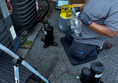 An HVAC technician kneeling on a mat works on a residential outdoor air conditioning unit.