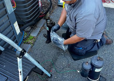 A technician wearing a hat and gloves repairs an outdoor HVAC unit.