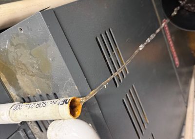 Water leaking from an open white PVC pipe onto a furnace.