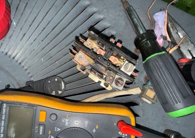 A faulty HVAC contactor, multimeter, and screwdriver resting on an outdoor air conditioner unit.