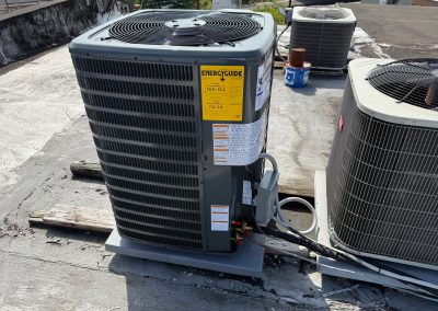 Three HVAC condenser units on a flat roof, with a visible yellow EnergyGuide label on the central unit.