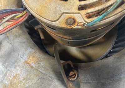 Close-up of a metal blower motor housing with wiring and a rusted mounting bracket.