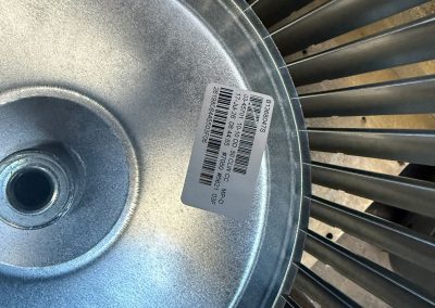 Metal blower wheel with a barcode sticker containing part numbers and manufacturing details.