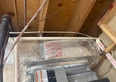 HVAC ductwork wrapped in foil insulation and electrical wiring located between exposed wooden floor joists.