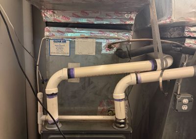 Goodman furnace unit with white PVC piping and connected metal ductwork.