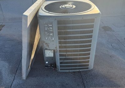 An outdoor air conditioning unit with a detached side panel on a flat roof.